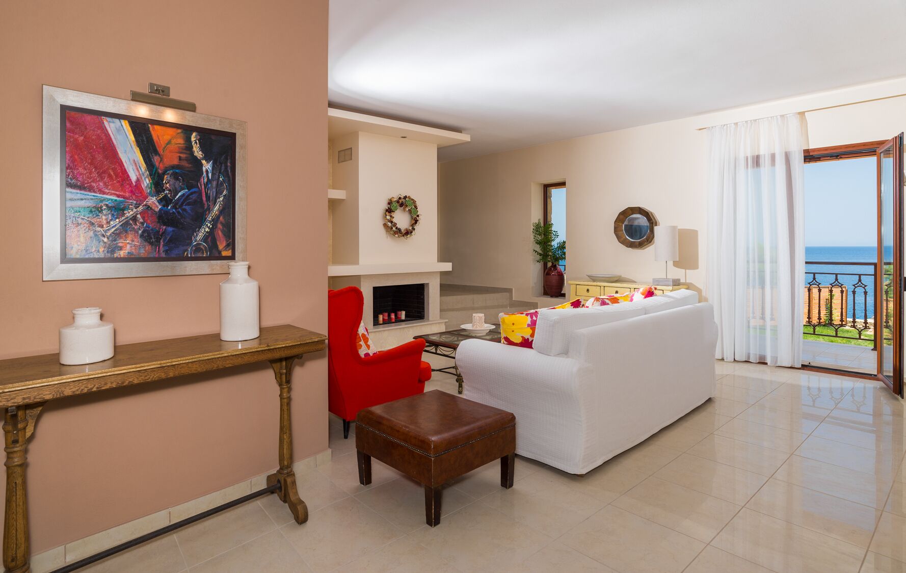 A living room with a white sofa, a red armchair, a wooden coffee table, a fireplace, and a large painting.