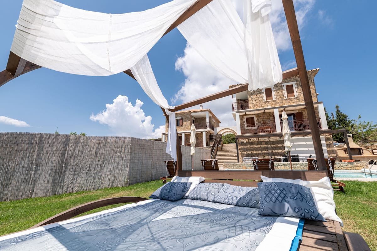 A bed with a canopy, a pool, and a stone building in the background.