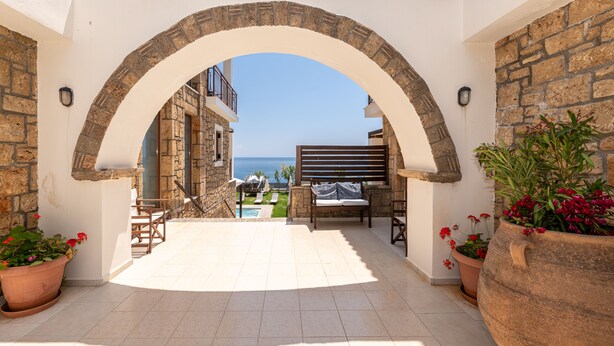 Un patio al aire libre con un arco de piedra, plantas en macetas y vistas al mar.