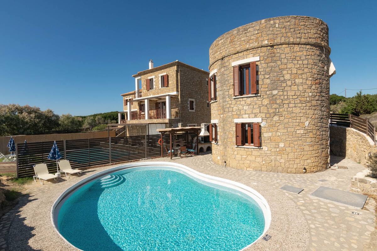 A stone building with a pool, outdoor seating, and a balcony.
