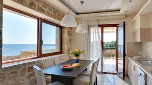 Un comedor con una mesa preparada para dos personas, un jarrón con flores y vistas al mar a través de amplios ventanales.