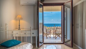 Un dormitorio con cama, escritorio y vista al océano a través de una puerta abierta.