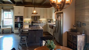 A spacious kitchen with wooden cabinets, a central island, and a large chandelier. - Sweets River Nest-riverfront/tube/hot tub/log cabin-fishing- Valle Crucis/App ST (Banner Elk)