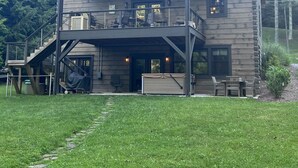 A two-story log cabin with a balcony, outdoor seating, and a covered patio area. - Sweets River Nest-riverfront/tube/hot tub/log cabin-fishing- Valle Crucis/App ST (Banner Elk)