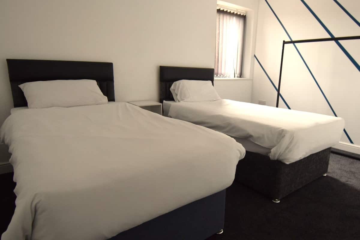 A hotel room with two beds, a window with curtains, and a geometric wall design.