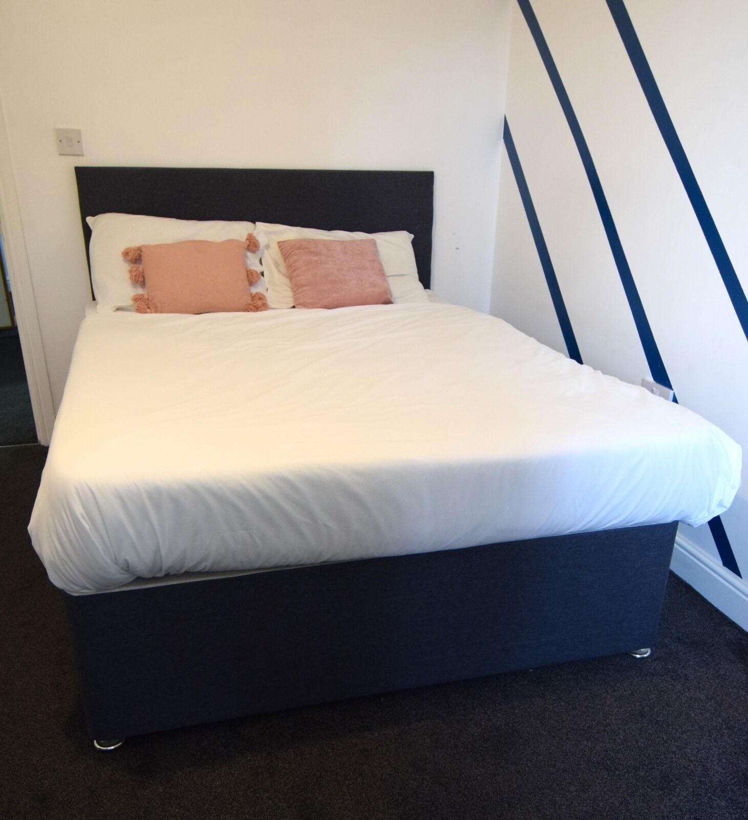 Una cama con estructura negra, ropa de cama blanca y dos almohadas.