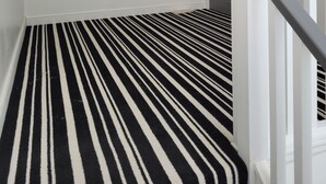 Ein Flur mit einem schwarz-weißen Streifen Teppich, einem roten Blumenbild an der Wand und einer weißen Tür mit grauem Rahmen.