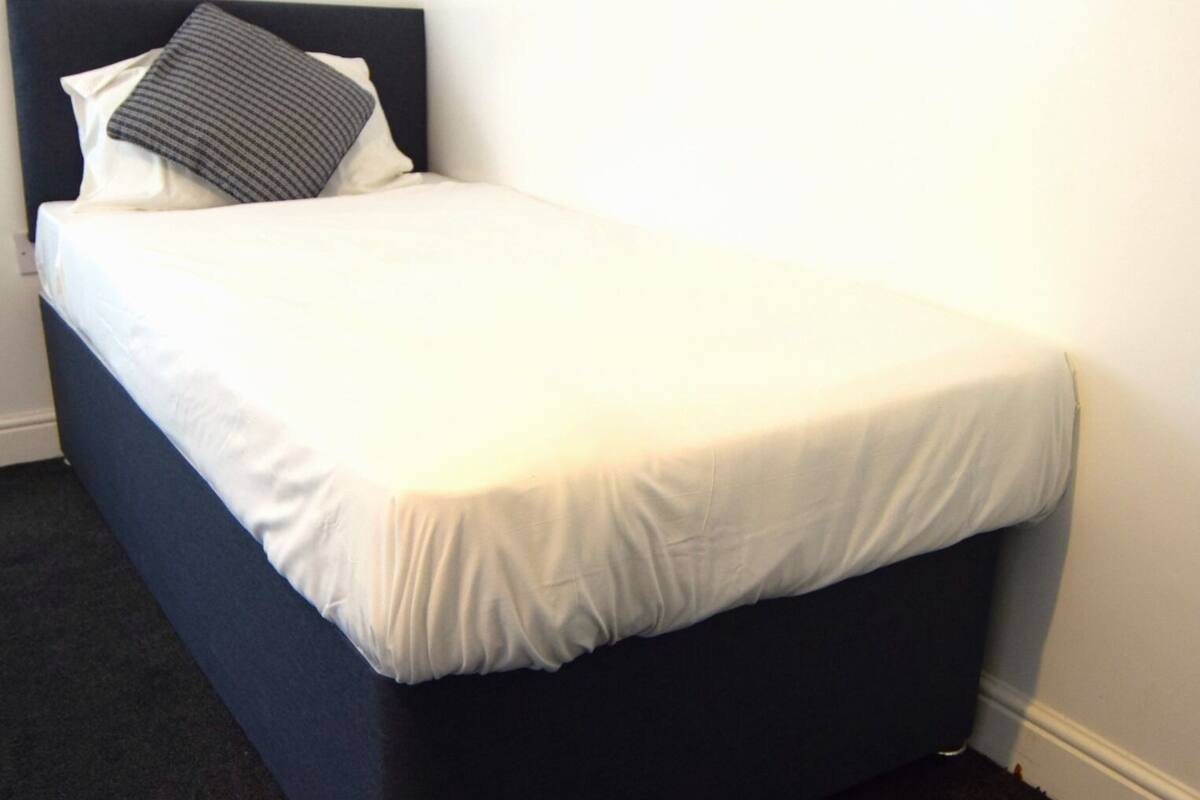 A single bed with a white mattress and a dark headboard.