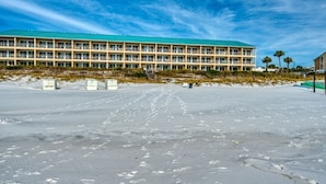 En stor, mangeetagers bygning med fladt tag og mange vinduer, beliggende på en sandstrand med fodaftryk, der fører hen til den.