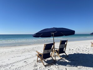 Une plage avec deux chaises de plage en bois et un grand parasol.