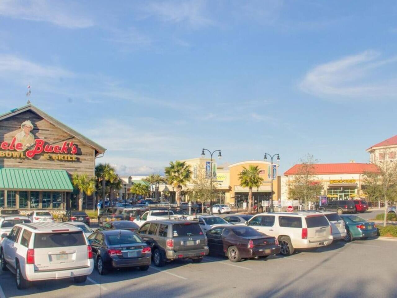 Un estacionamiento con varios coches, un restaurante llamado 'Bowl Buck's' y un centro comercial al fondo.