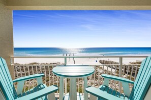 A balcony with two turquoise chairs and a small table, overlooking a beach with a clear blue sky and calm sea. - Salty Dolphin -  Gulf Front Oasis on Crystal Beach (Destin)