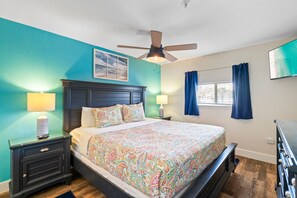 Une chambre avec des murs de couleur turquoise, un cadre de lit en bois, un ventilateur de plafond et un téléviseur fixé au mur.