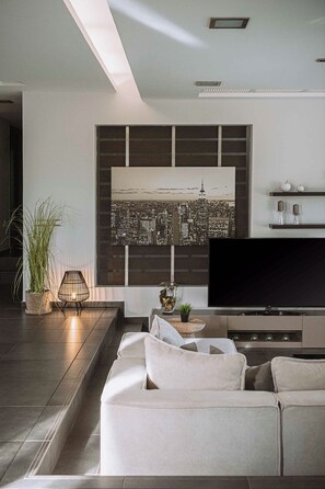 A modern living room with a large flat-screen TV, a sofa, a decorative wall with a cityscape, and a small plant.
