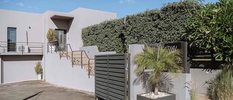 Un bâtiment moderne doté d’une entrée sécurisée par un portail, d’un escalier et d’une haie bien entretenue.