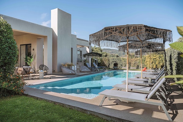 A modern outdoor pool area with lounge chairs, a pergola, and a view of the surrounding landscape. - Villa Vega (Platanias)