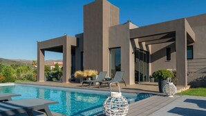 Un edificio moderno con piscina, poltrone relax e vista libera sul paesaggio circostante.