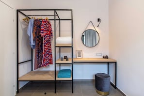Una habitación compacta con un armario de metal, un espejo redondo, una mesita con un marco de fotos y un taburete.