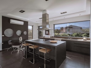 Una cocina moderna con una isla central, taburetes de bar y un amplio ventanal con vistas al exterior.