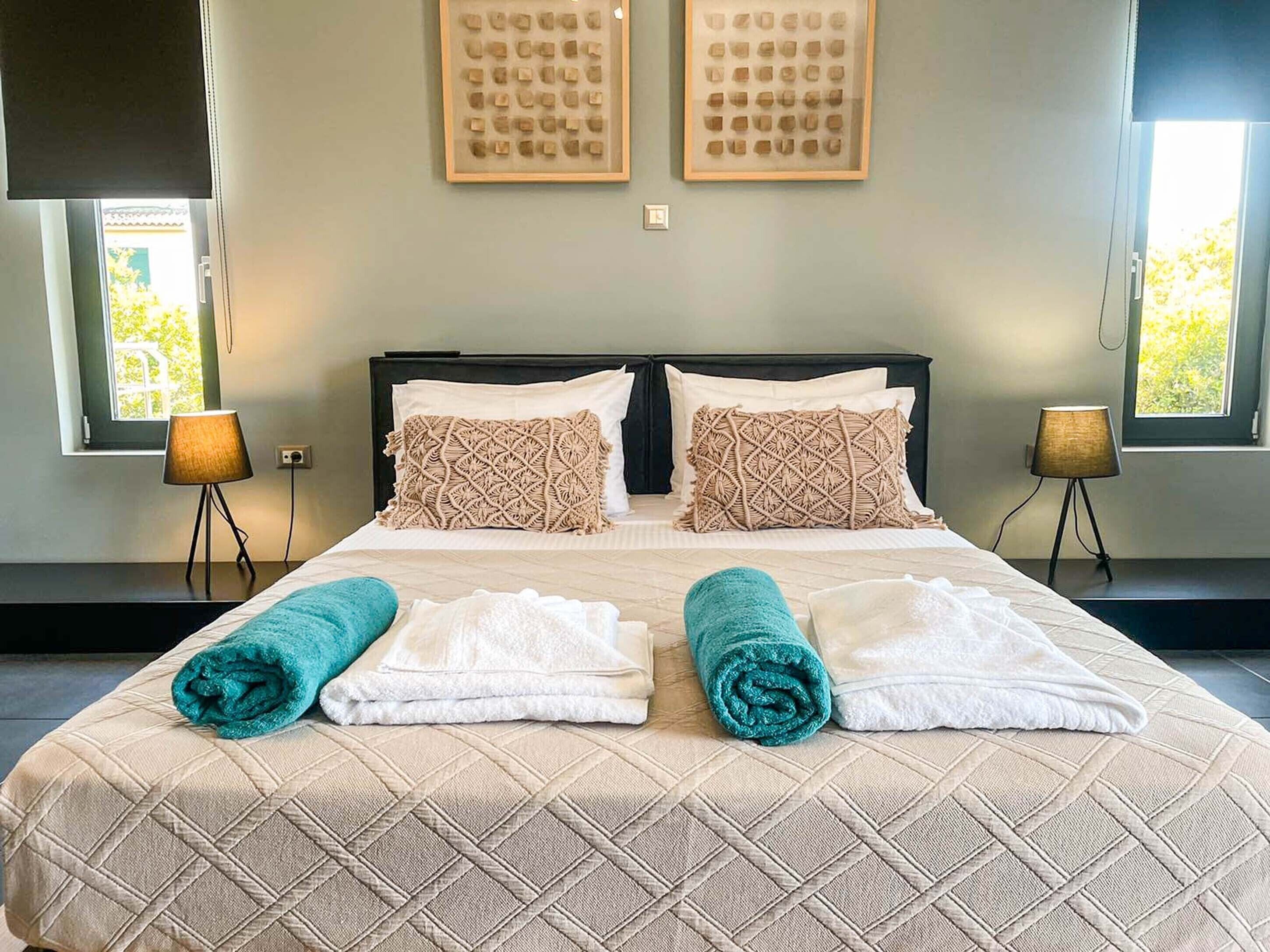 A double bed with a quilted headboard, two bedside lamps, and a window with a view of greenery.