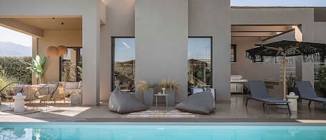 Un espace moderne aménagé au bord de la piscine, comprenant une piscine, des chaises longues et un barbecue.