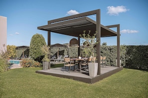 An outdoor patio area with a pergola, seating, and a pool. - Villa Vega (Platanias)