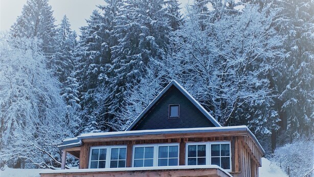 A wooden cabin with a balcony, surrounded by snow-covered trees.