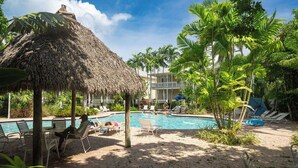 A pool area with lounge chairs, a thatched umbrella, and palm trees.