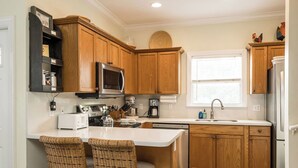 A kitchen with wooden cabinets, a microwave, a coffee maker, and a sink. There are two wicker chairs at the island.