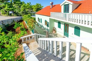 A two-story building with a red roof, white walls, and green shutters. There is a stone wall and a small garden area with plants. - Seafront Holiday Home Marija (Blato)