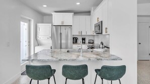 A modern kitchen with white cabinets, stainless steel appliances, and a marble countertop. - The Palm Leaf 3 Bedroom Home by RedAwning (Anna Maria)