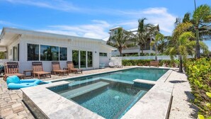 A rectangular swimming pool with a tiled edge, surrounded by a concrete deck. There are wooden lounge chairs and a blue inflatable float. - The Palm Leaf 3 Bedroom Home by RedAwning (Anna Maria)