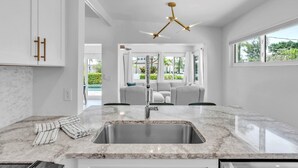 A modern kitchen with a marble countertop, stainless steel sink, and a unique ceiling fan. - The Palm Leaf 3 Bedroom Home by RedAwning (Anna Maria)