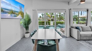 A modern living room with a dining table, a sofa, and a large window overlooking a pool and outdoor area. - The Palm Leaf 3 Bedroom Home by RedAwning (Anna Maria)