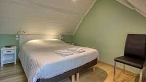 Une chambre à coucher avec un lit, une chaise, une table de chevet et une lampe.