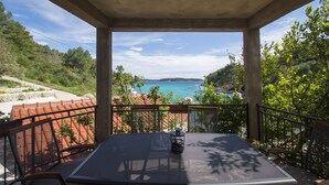 A balcony with a table and chairs, overlooking a coastal landscape with trees and a view of the sea. - Apartment Slatina (Vela Luka)