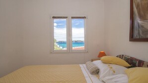 A bedroom with a bed, a window with a view of the sea, and a painting on the wall. - Apartment Slatina (Vela Luka)
