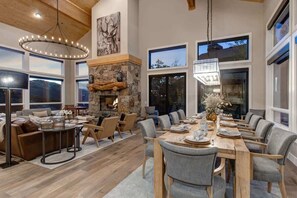 A spacious living area with a stone fireplace, a dining table set for six, and a large window offering a view of the outdoors.