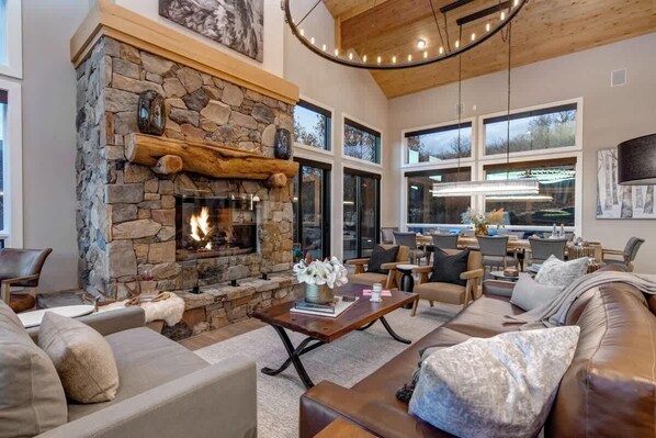 A spacious living room with a stone fireplace, leather sofas, and a dining area with large windows.