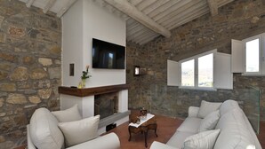 A stone-walled room with a fireplace, white sofas, and a television mounted on the wall. - Gittori, Gaiole in Chianti, Siena and Chianti (Gaiole in Chianti)