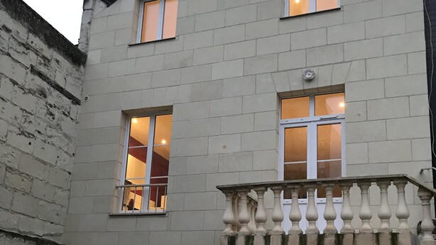 A two-story building with a stone facade, multiple windows, and a small balcony with balustrades.