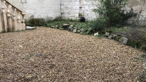 A courtyard with a gravel path, a stone wall, and a staircase.