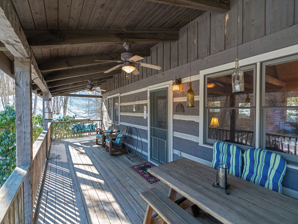 A covered outdoor deck with wooden benches and tables, a ceiling fan, and hanging pendant lights.
