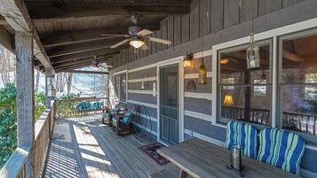 A covered outdoor deck with wooden benches and tables, a ceiling fan, and hanging pendant lights.