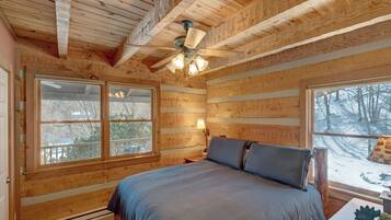 A wooden cabin bedroom with a bed, a ceiling fan, and large windows.