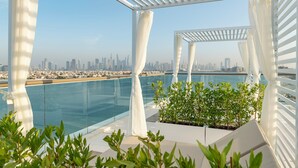 Une terrasse sur le toit dotée d’une piscine à débordement en verre, d’une pergola blanche et offrant une vue panoramique sur la ville.