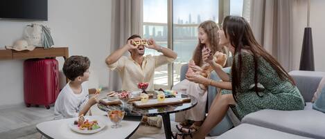 A modern living room with a city view, a round table with food, and a red suitcase.