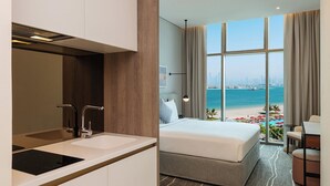 A hotel room with a large bed, a desk, and a view of the beach and city skyline. - Th8 Palm Dubai Beach Resort, Vignette Collection by IHG (Dubai)