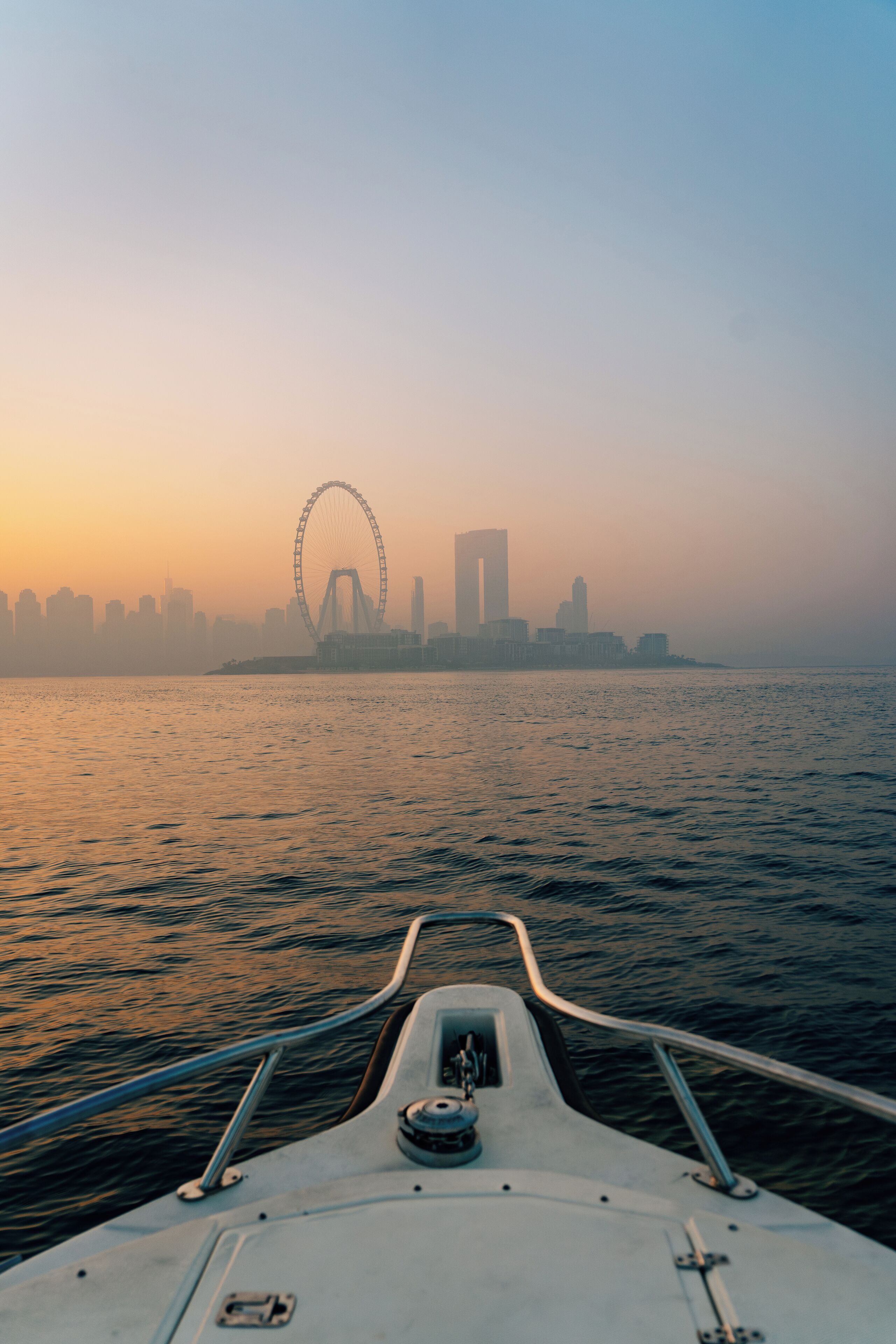 La proa de un barco con vistas a un horizonte urbano y una noria grande a lo lejos.