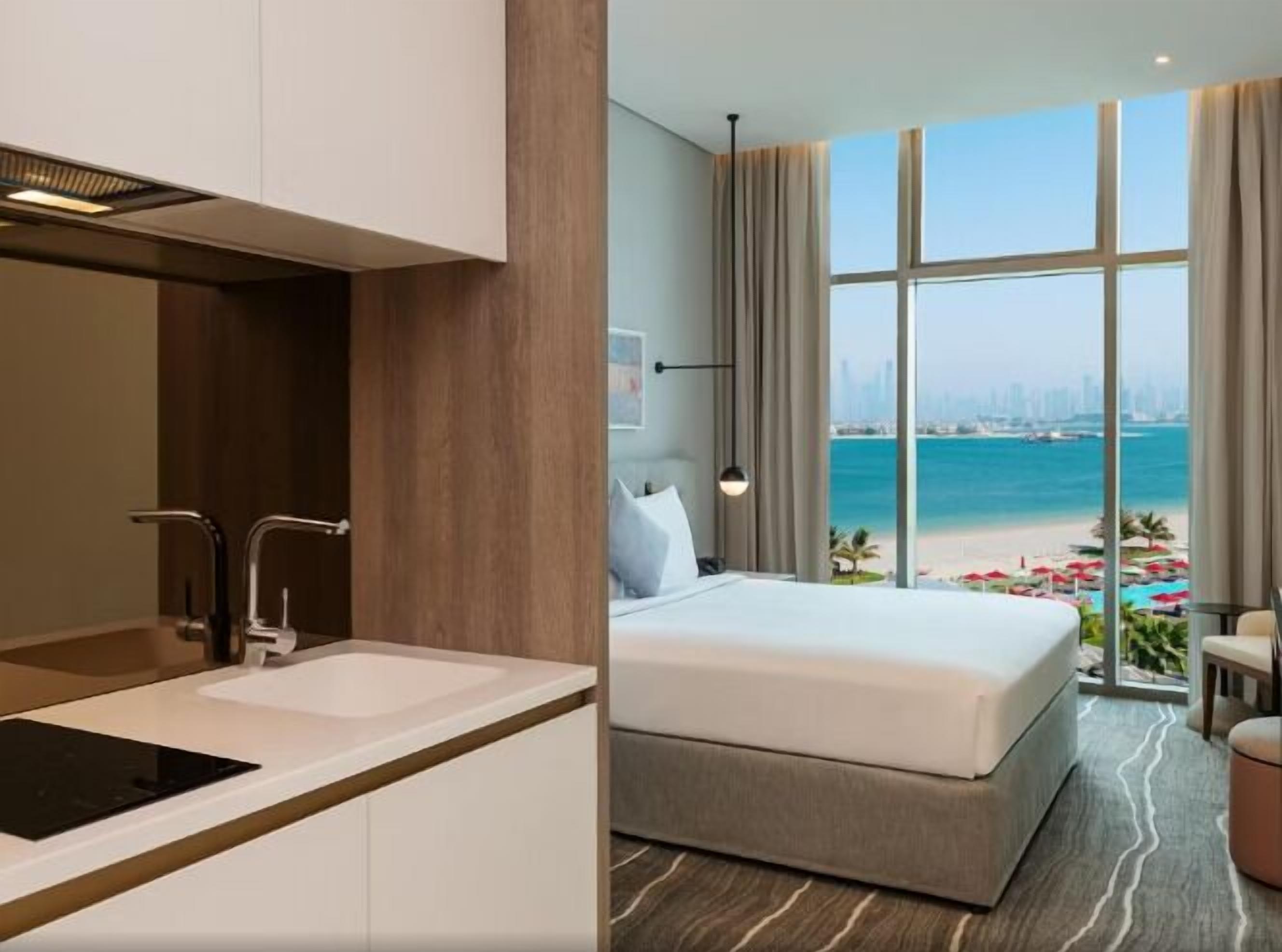 Une chambre d’hôtel moderne dotée d’un grand lit, offrant une vue sur la plage, et comprenant une salle de bain séparée.